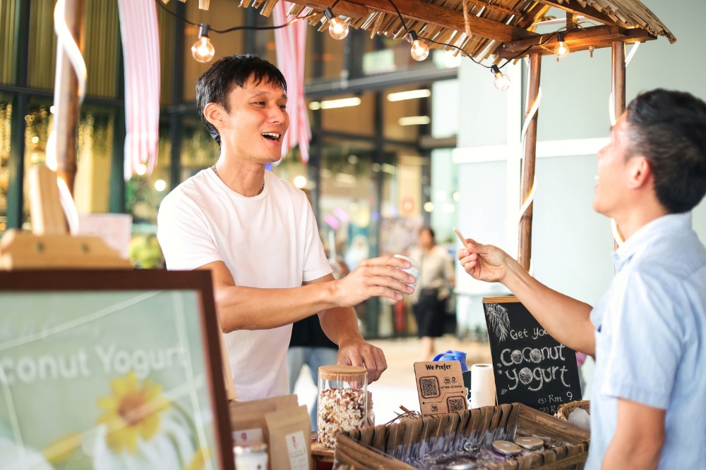 Gutsuka founder serving fresh plant-based coconut yogurt to a customer at a local Malaysia marketplace booth.