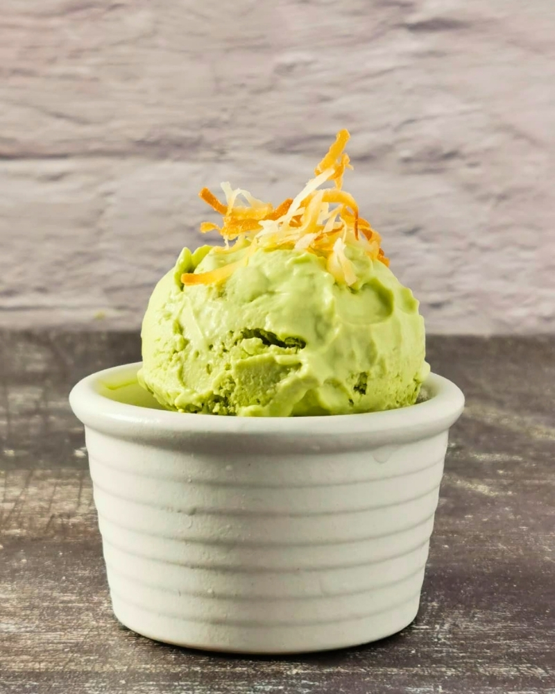 A scoop of creamy avocado dairy-free coconut yogurt ice cream in a white ramekin, topped with toasted coconut flakes.