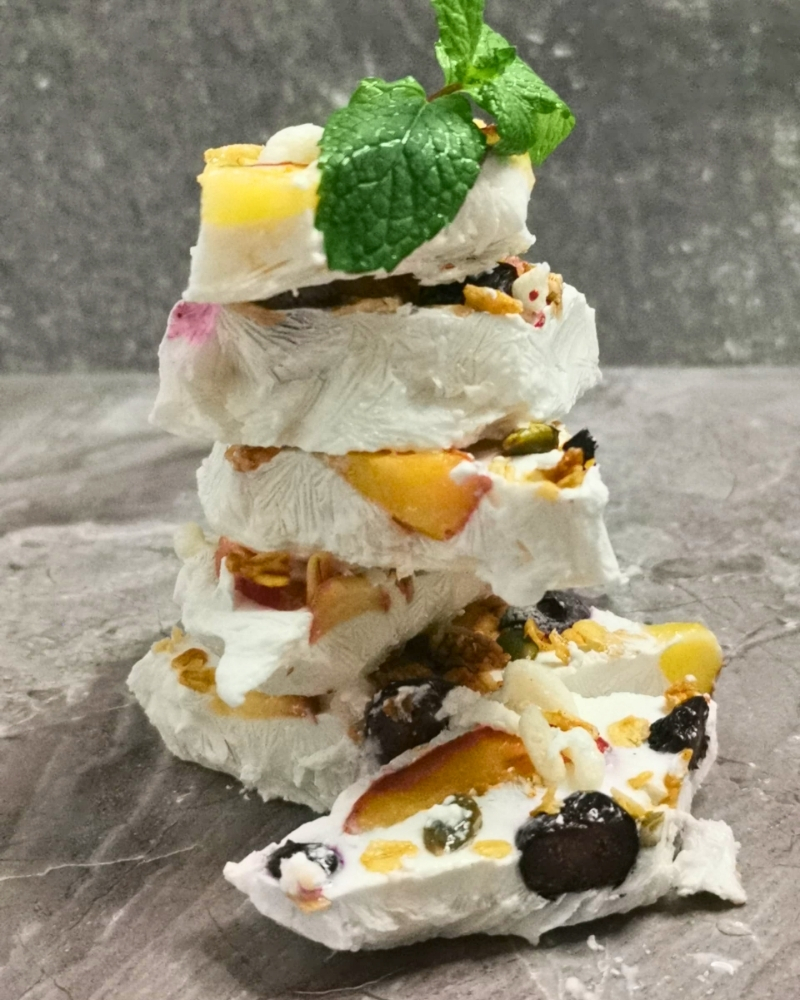 Fruity Frozen Yogurt Bark Recipe A stack of frozen yogurt bark made with Gutsuka coconut yogurt, topped with fresh berries, sliced peaches, and granola.