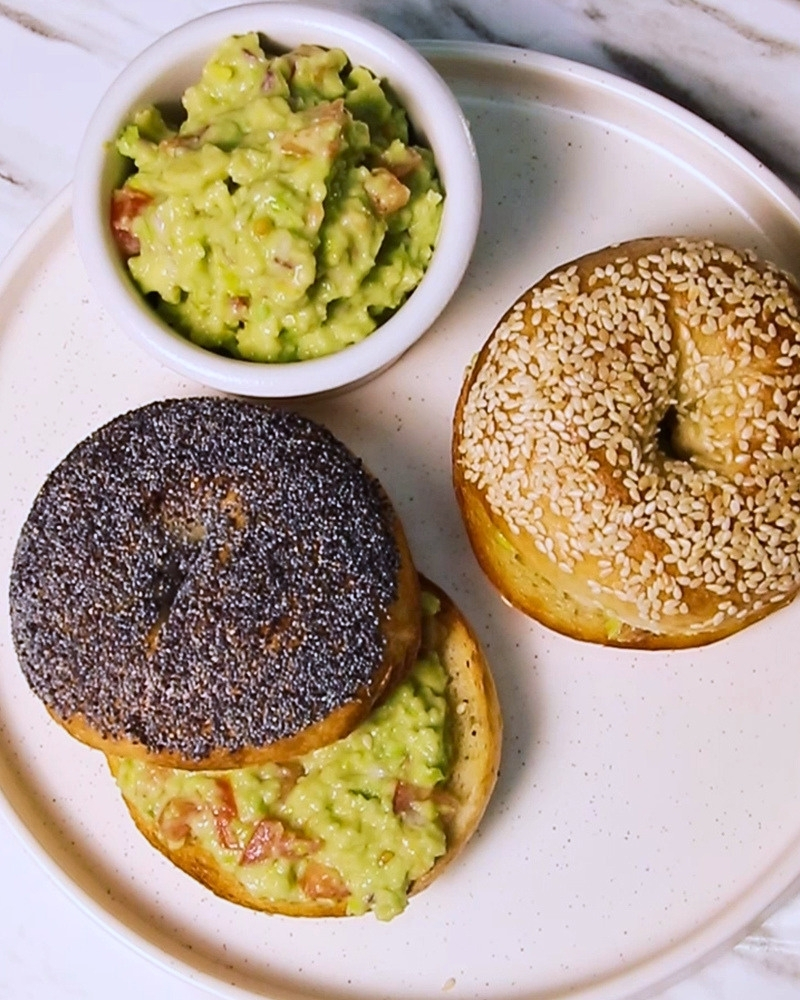 A bowl of fresh guacamole made with coconut yogurt served alongside toasted sesame and poppy seed bagels.